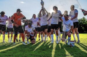 Spieler des FC Wehr 1912 feiern mit Pokal und Getränkedusche auf dem Sportplatz bei Gegenlicht