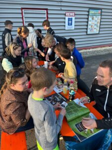 Kinder und Eltern sammeln gemeinsam Sticker des StickerStars-2026-Projekts vor einem REWE-Markt