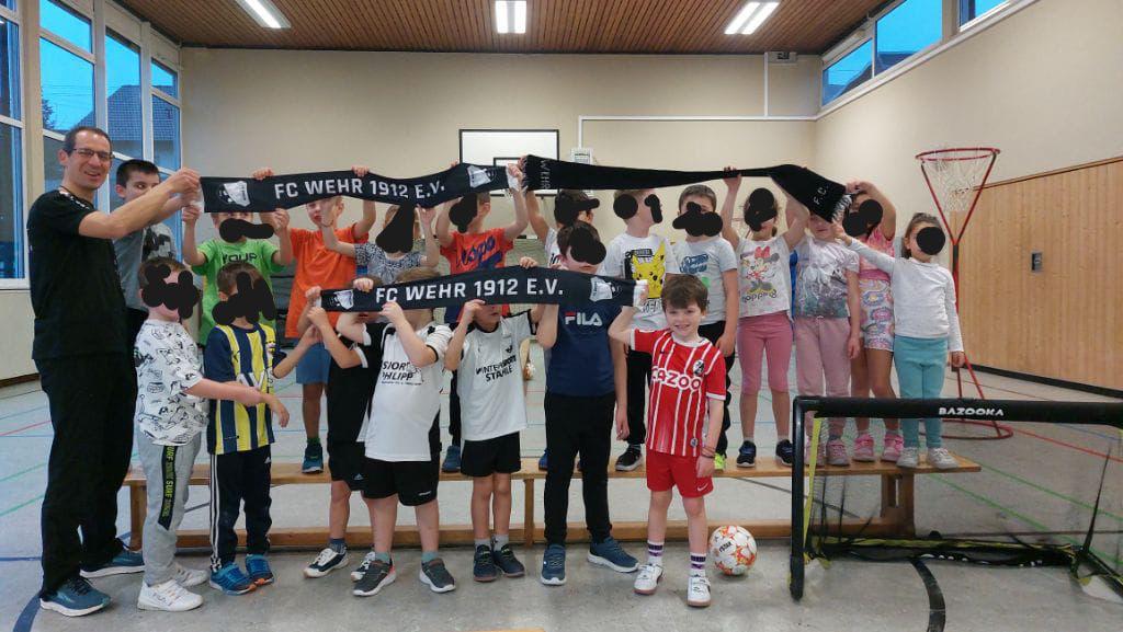 Gruppe von Kindern hält gemeinsam FC-Wehr-1912-Schals in einer Sporthalle hoch