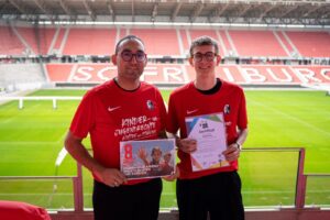 Zwei Träger mit Kindertrainer-Zertifikat und Aktion 'Kinder- und Jugendrechte achten und stärken' im Stadion des SC Freiburg