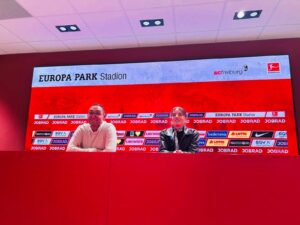 Zwei Personen sitzen am Pressekonferenztisch des Europa-Park Stadions mit SC-Freiburg-Logo